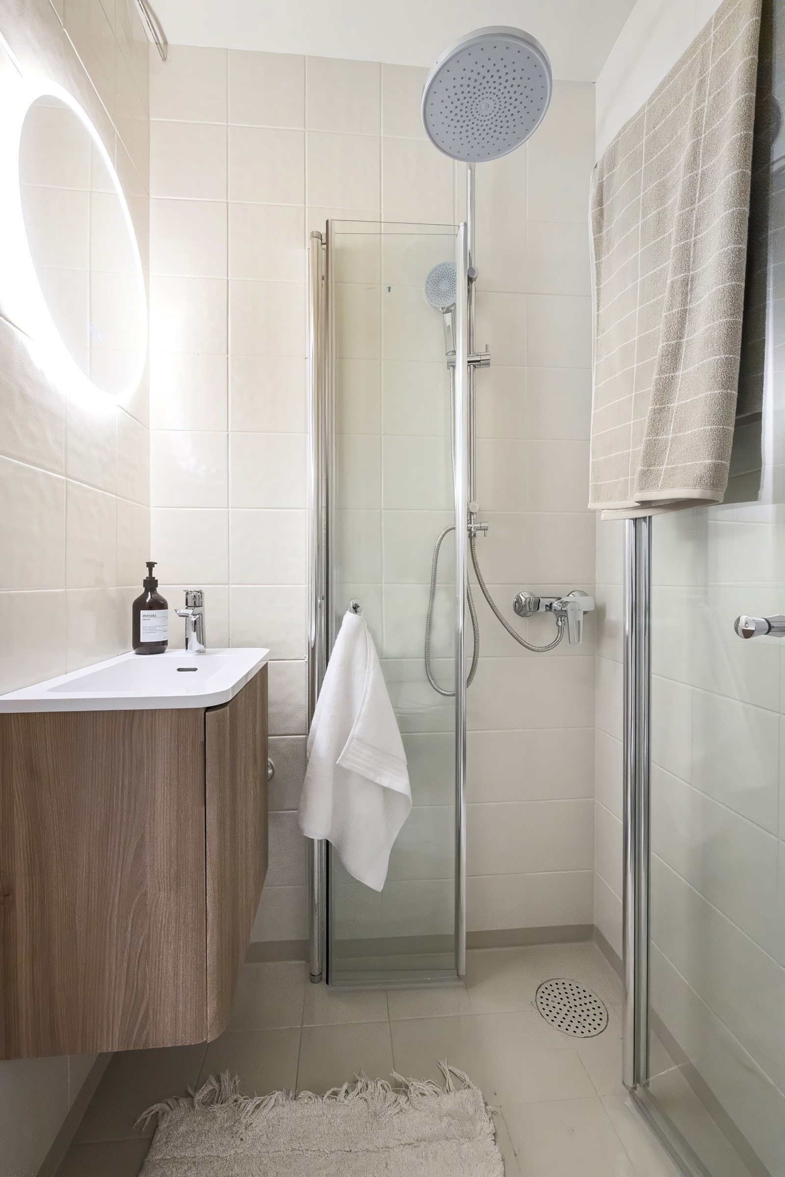 Badet fremstår lyst og pent, med flislagte overflater og en praktisk planløsning. Det er innredet med dusjhjørne med innfellbare glassdører, moderne servantinnredning med god oppbevaring og rund lysende speil. Galleribilde