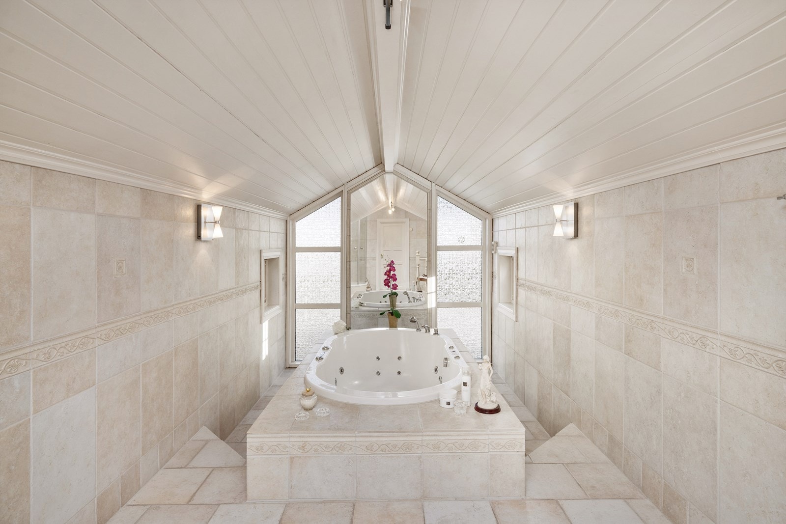 En trapp leder opp til et lekkert, forhøyet område med et innbydende badekar med speil i bakkant. Et delikat og harmonisk bad som gir en følelse av velvære i hverdagen. Galleribilde