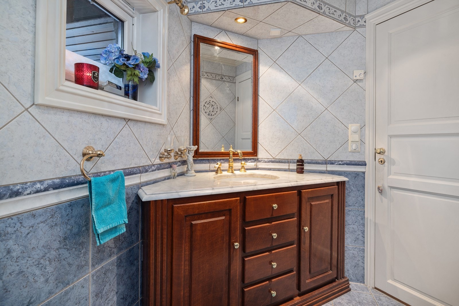 Badet har elegante lyse fliser med vannbåren gulvvarme. Det solide baderomsmøbelet i mørkt tre tilfører varme og tyngde, mens benkeplaten i lys marmor gir en eksklusiv kontrast. Galleribilde