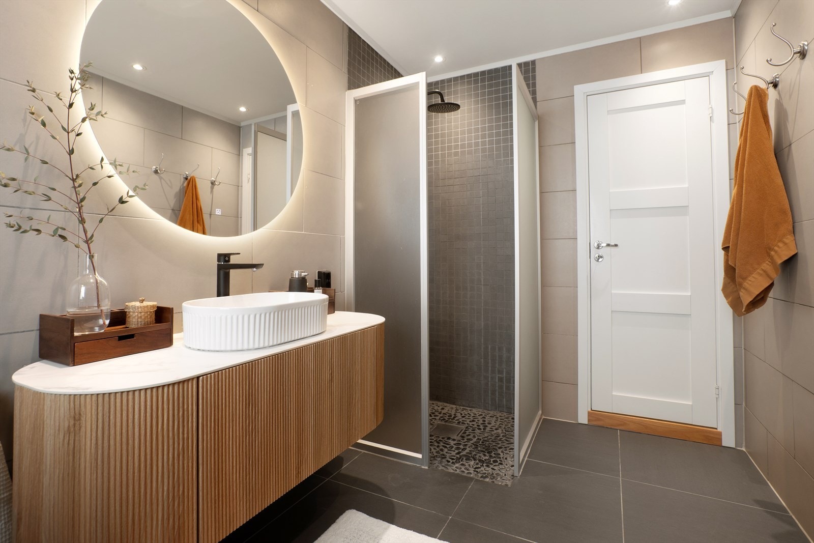 Badet er utstyrt med stilren innredning med servantbolle, speil med lys, toalett og dusjnisje med regndusj Galleribilde