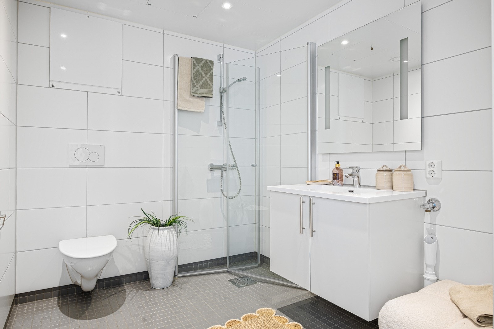 Moderne baderom fra byggeåret 2018, med fliser på gulv og vegger, vegghengt toalett og opplegg for vaskemaskin. Galleribilde