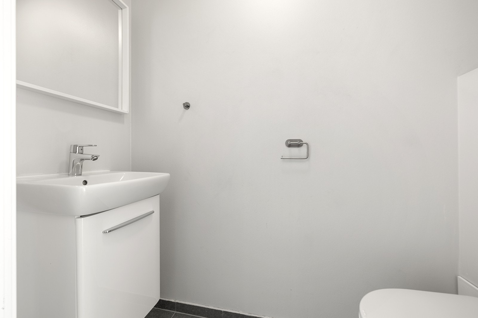 Separat toalett med flislagt gulv og malte overflater. Vegghengt toalett og servant med skap. Galleribilde