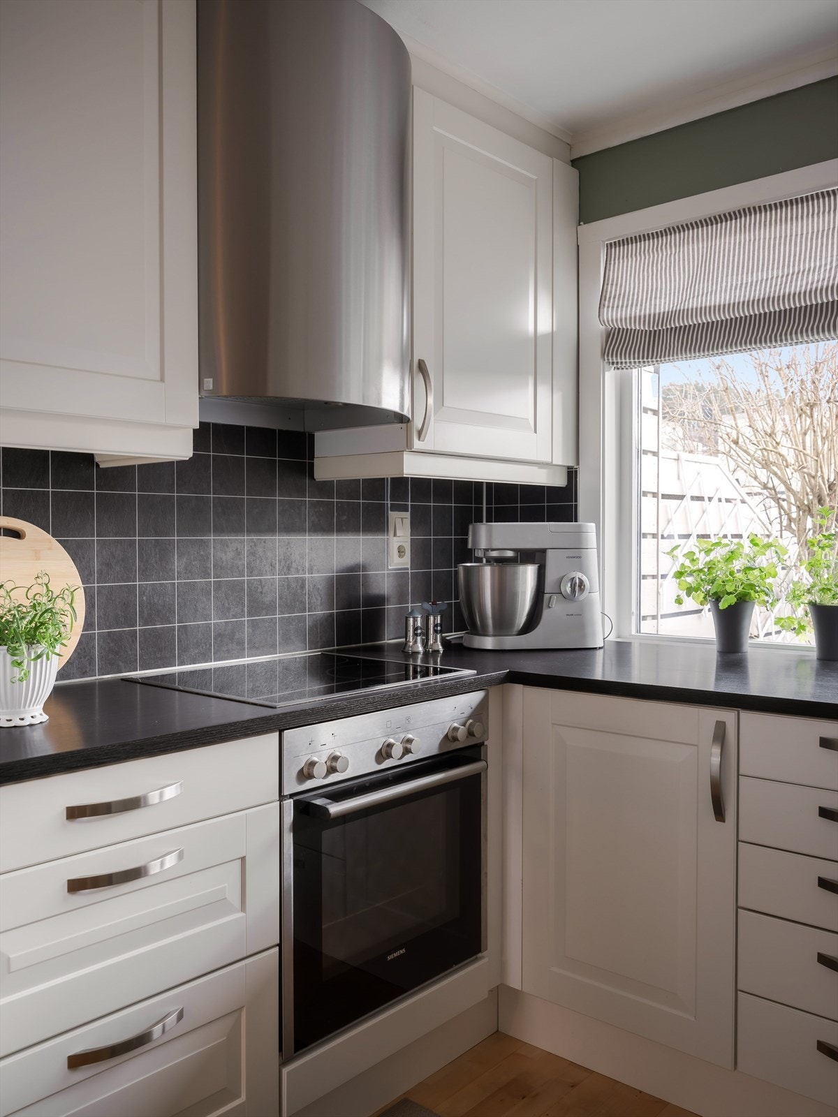 Her er det praktiske fliser over benkeplatene og overskapene går helt opp til taket. Stålfarget ventilator og godt arbeidslys over kjøkkenbenken. Galleribilde