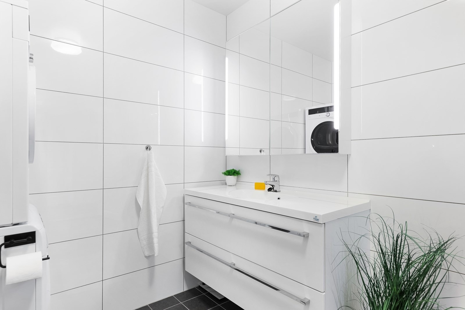 Badet er innredet med vegghengt toalett, dusjhjørne med glassdører samt vegghengt servantskap med overliggende servant Galleribilde