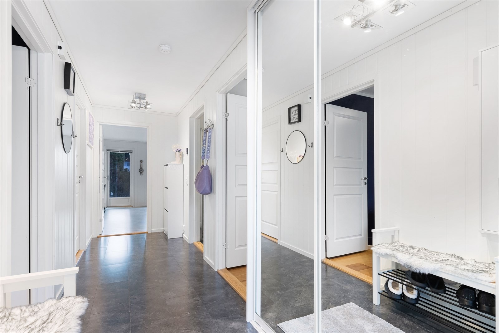 Lys og romslig entré med laminat på gulv, lysmalte vegger og praktisk skyvedørsgarderobe med speil, samt god plass til yttertøy og sko. Galleribilde