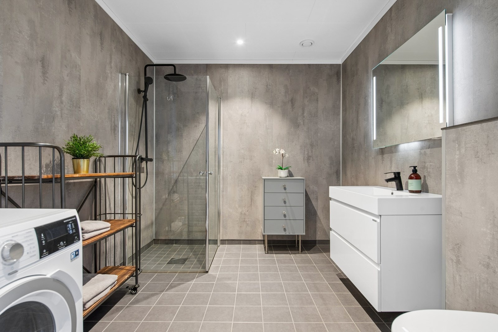 Romslig bad med flislagt gulv med gulvvarme, dusjhjørne med glassvegger og opplegg for vaskemaskin. Galleribilde