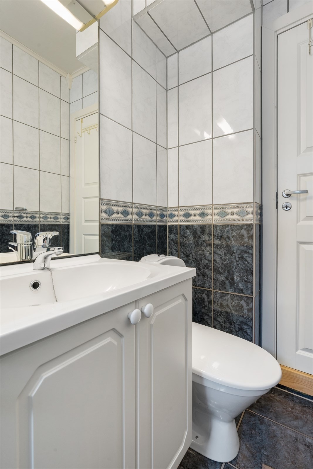 Hvit baderomsinnredning med profilerte fronter og gulvmontert toalett. Galleribilde