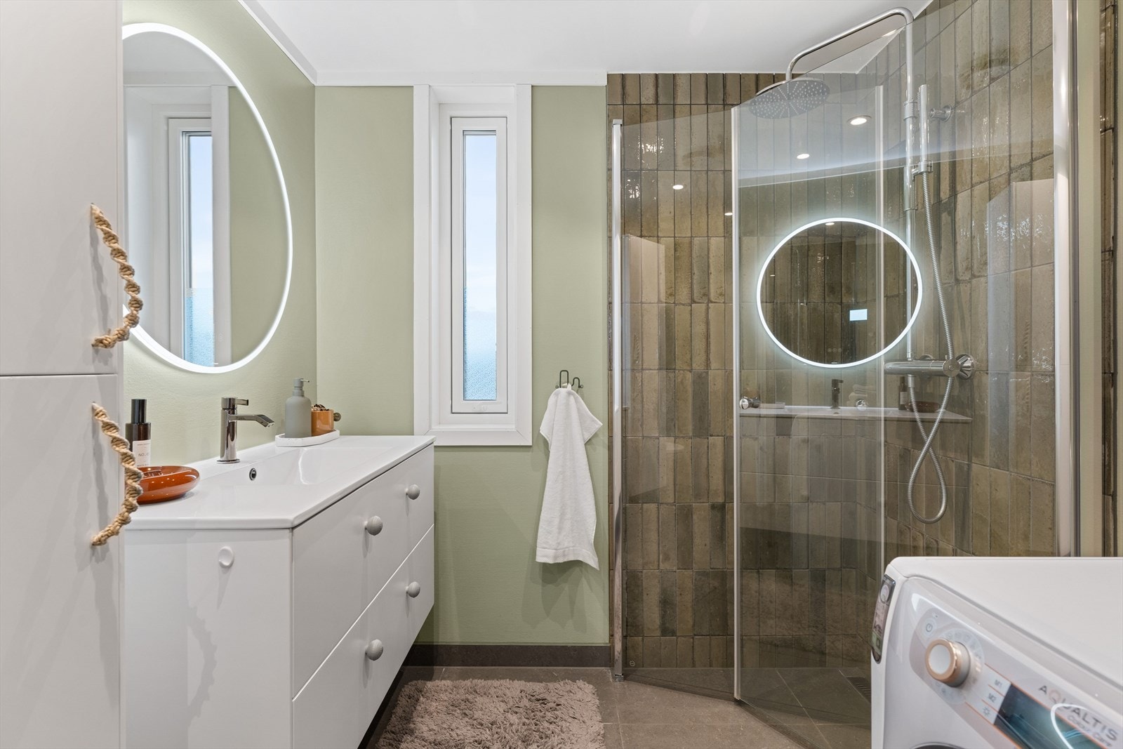 Videre er badet utstyrt med behagelig varmekabler i gulvet, dusjhjørne med innfellbare dører, vegghengt toalett og opplegg for vaskemaskin. Galleribilde