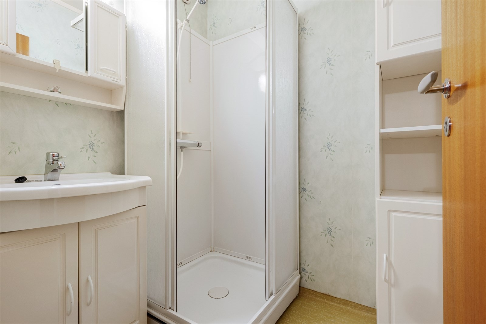 Badet er innredet med dusjkabinett, servant med tilhørende møblement, samt overskap med speil og lysarmatur Galleribilde