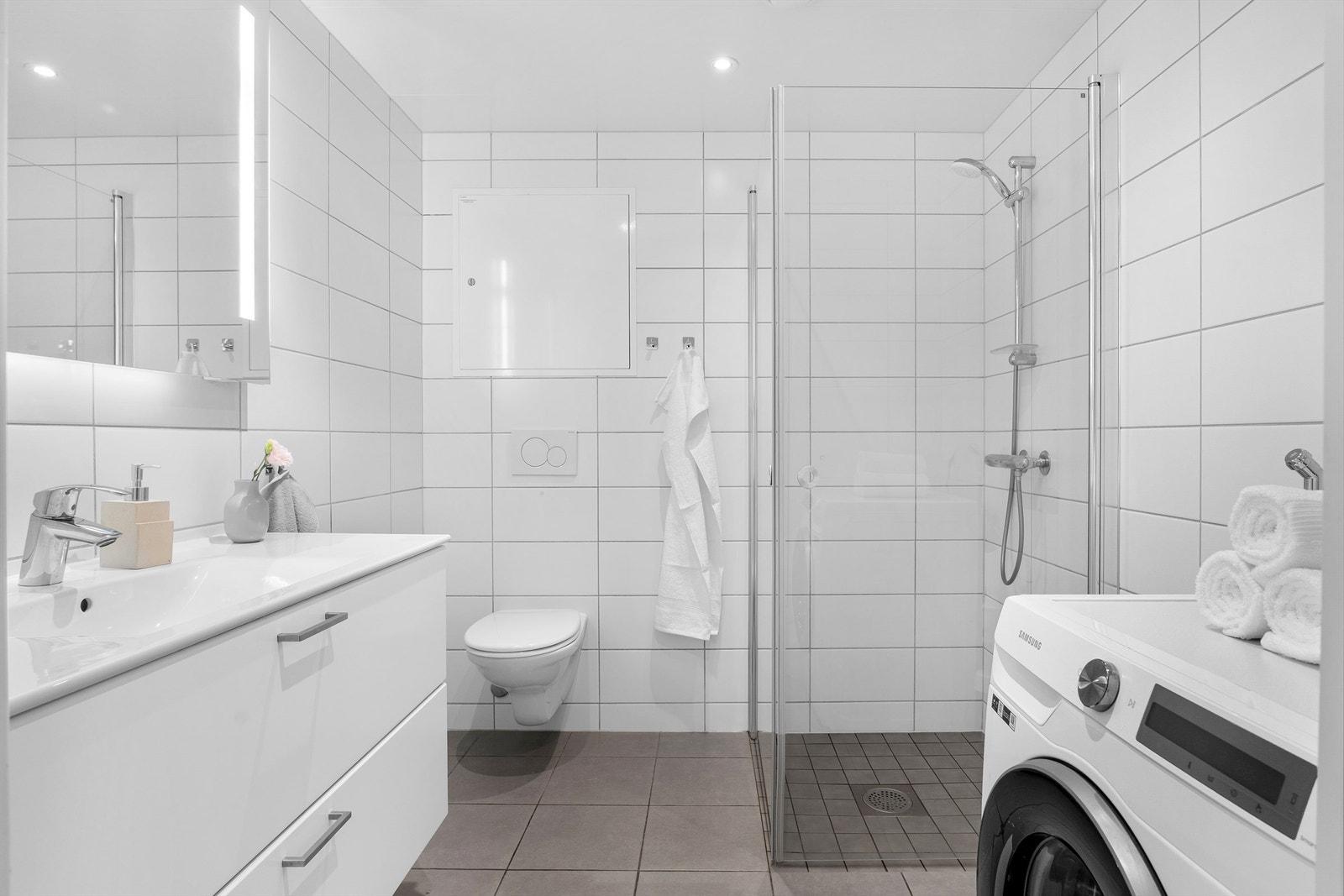 Boligens hovedbaderom er innbydende med grå fliser på gulv og hvite fliser på vegg. Opplegg for vaskemaskin. Galleribilde