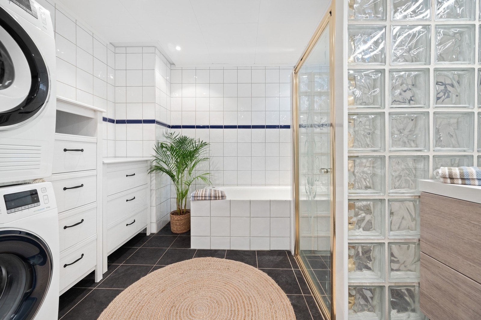 Stort bad i midtre plan med både dusj og innmurt badekar samt opplegg/plass for vaskemaskin og tørketrommel i søyle Galleribilde