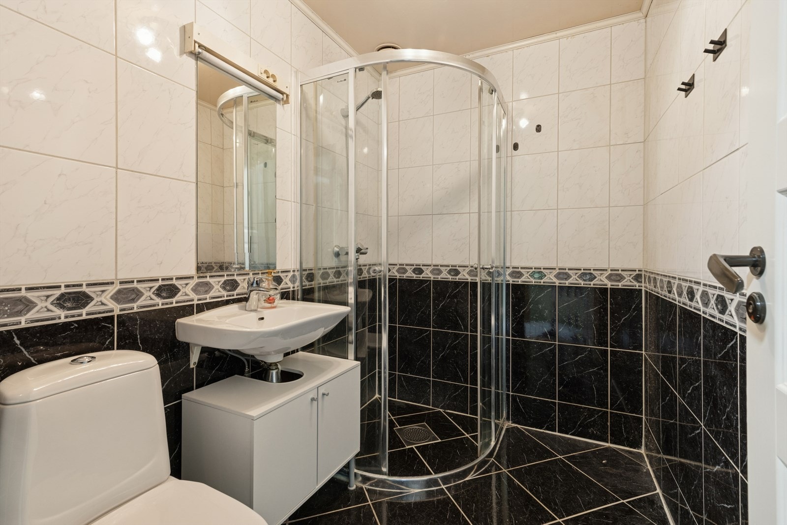 Flislagt baderom med elektriske varmekabler i gulv og malt himling. Badet er innredet med gulvstående toalett, dusjhjørne med dusjvegger samt vegghengt servant med et praktisk skap under. Galleribilde