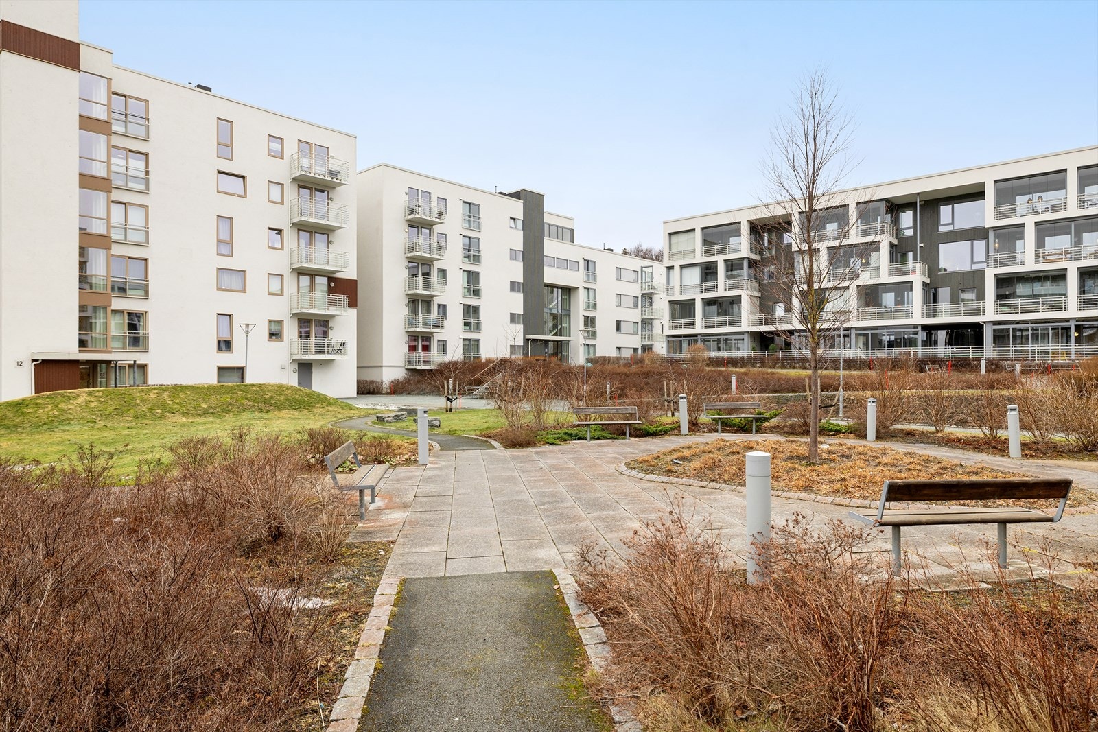 Fasadebilde av bygget som ligger i et moderne og attraktivt boligområde på Lade, omgitt av pent opparbeidede grøntområder og hyggelige sitteplasser. Galleribilde