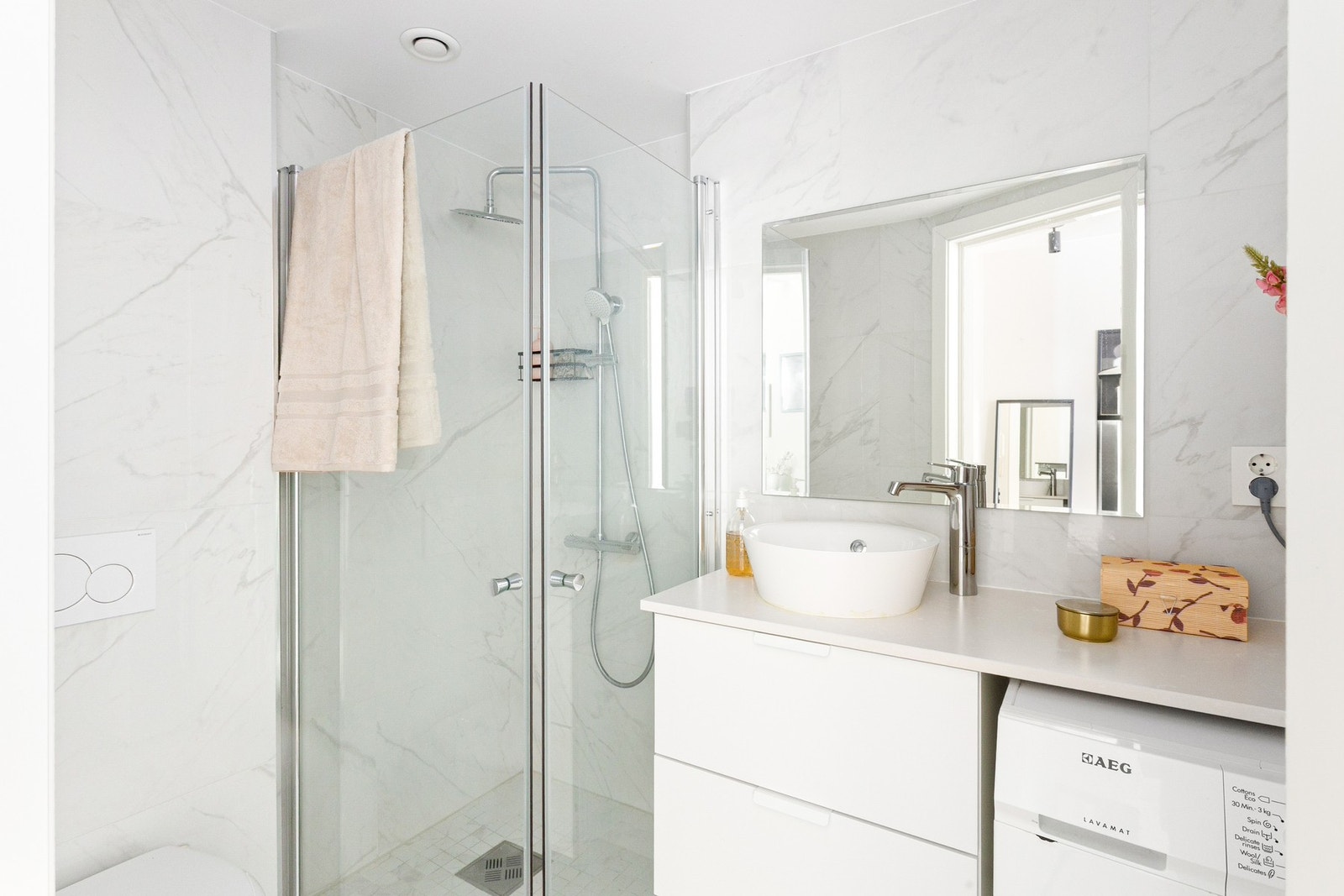 Lyst bad med dusjhjørne, vegghengt toalett og opplegg for vaskemaskin. Galleribilde