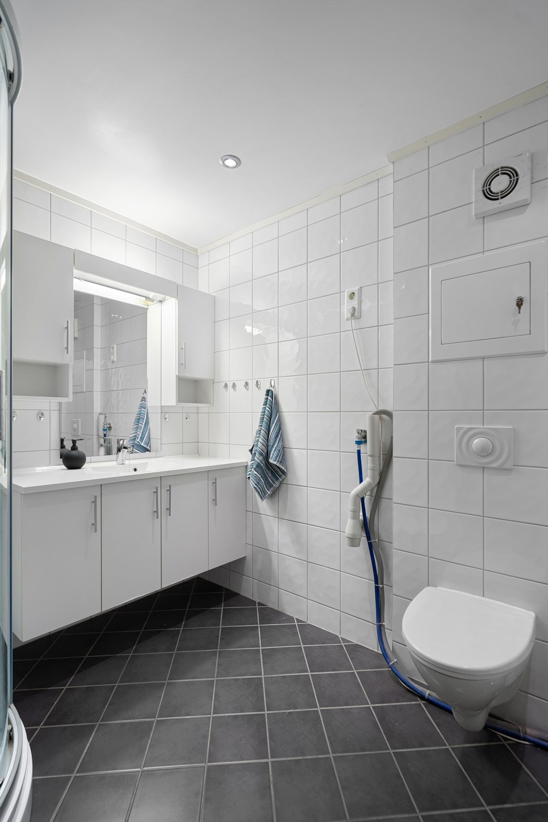 Stort flislagt bad i underetasje med vegghengt toalett, servant med skap, speil, overskap og dusjkabinett Galleribilde