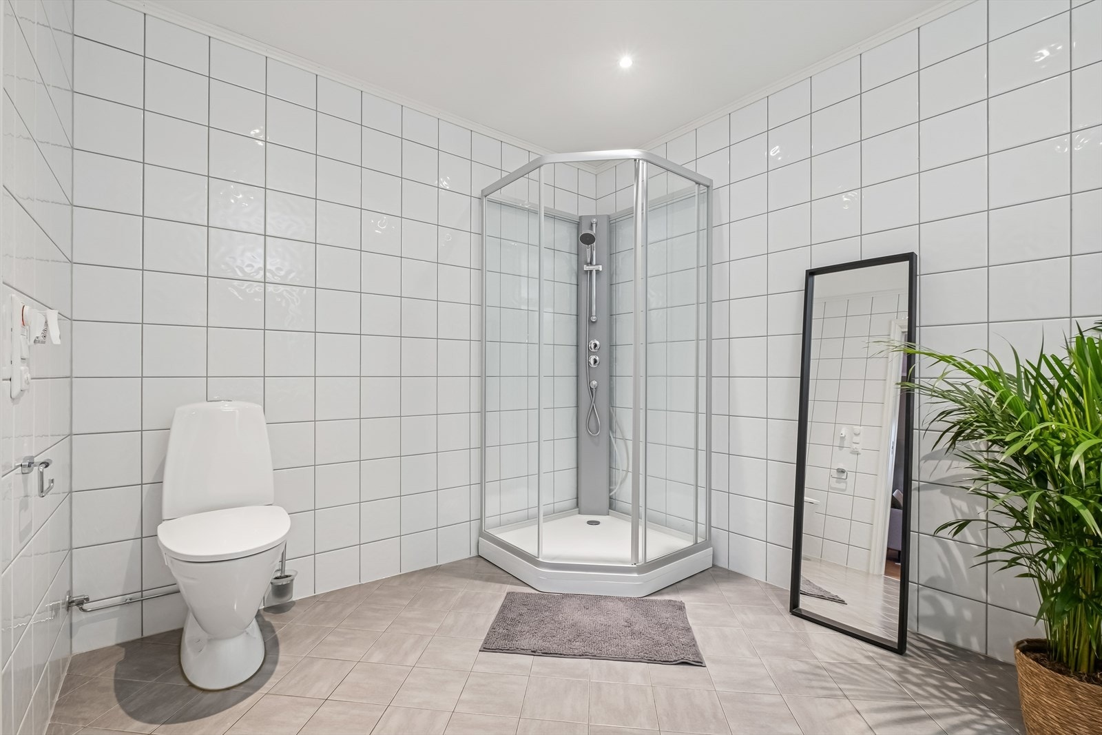 Badet er innredet med en hvit baderomsinnredning, speil, overskap, et gulvmontert toalett og dusjkabinett. Galleribilde