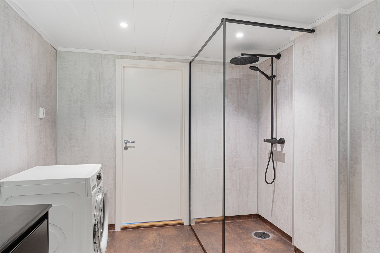 Badet er innredet med sort baderomsinnredning, vegghengt toalett, dusjnisje med glassvegg samt opplegg for vaskemaskin Galleribilde