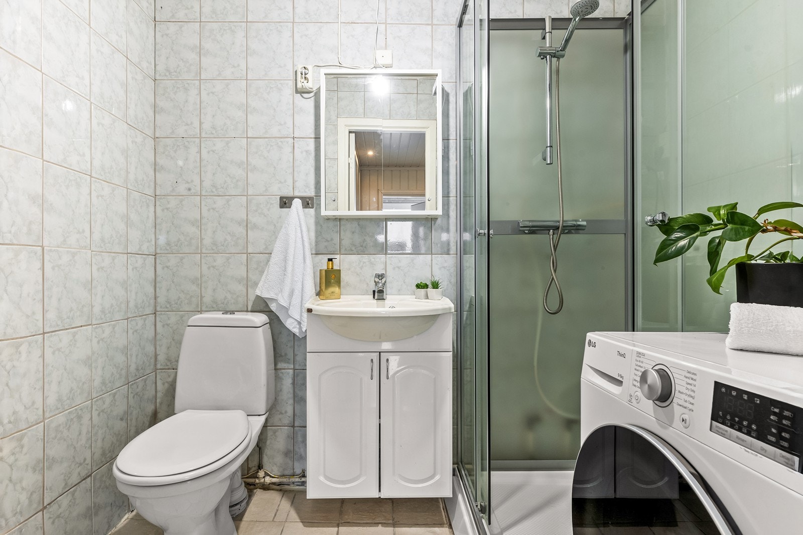 Badet har fliser på gulv og vegger, og er utstyrt med dusjkabinett og opplegg for vaskemaskin. Galleribilde