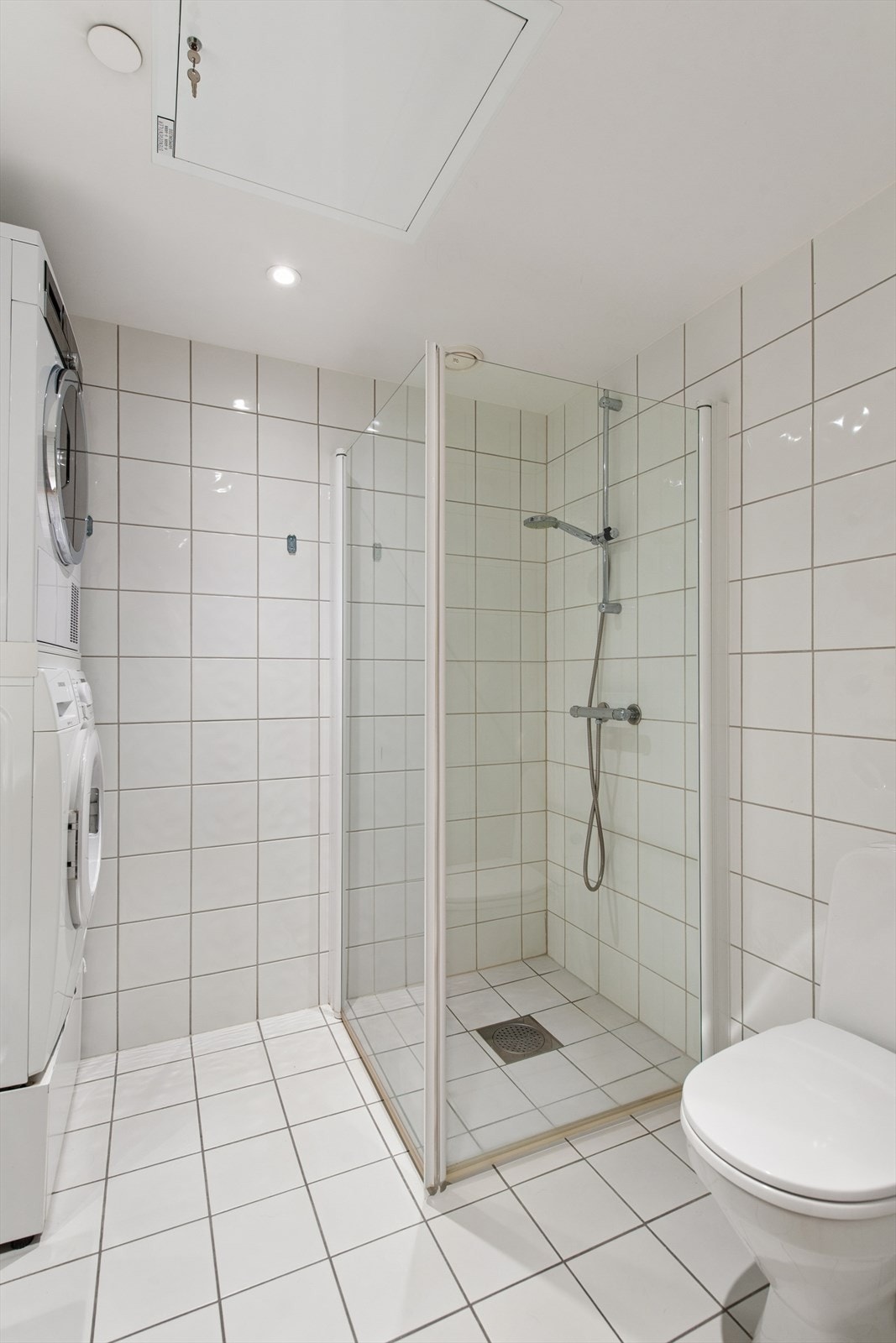 Det er dusjvegger, uttak til vaskemaskin, toalett og innredning med vask samt overskap på badet Galleribilde