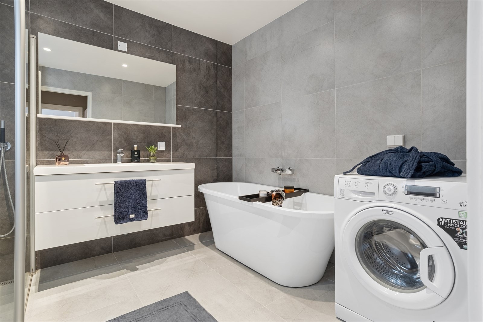 Badet er utstyrt med dusj, vegghengt toalett, badekar, vaskemaskin og baderomsinnredning med heldekkende servant og tilhørende speil. Galleribilde