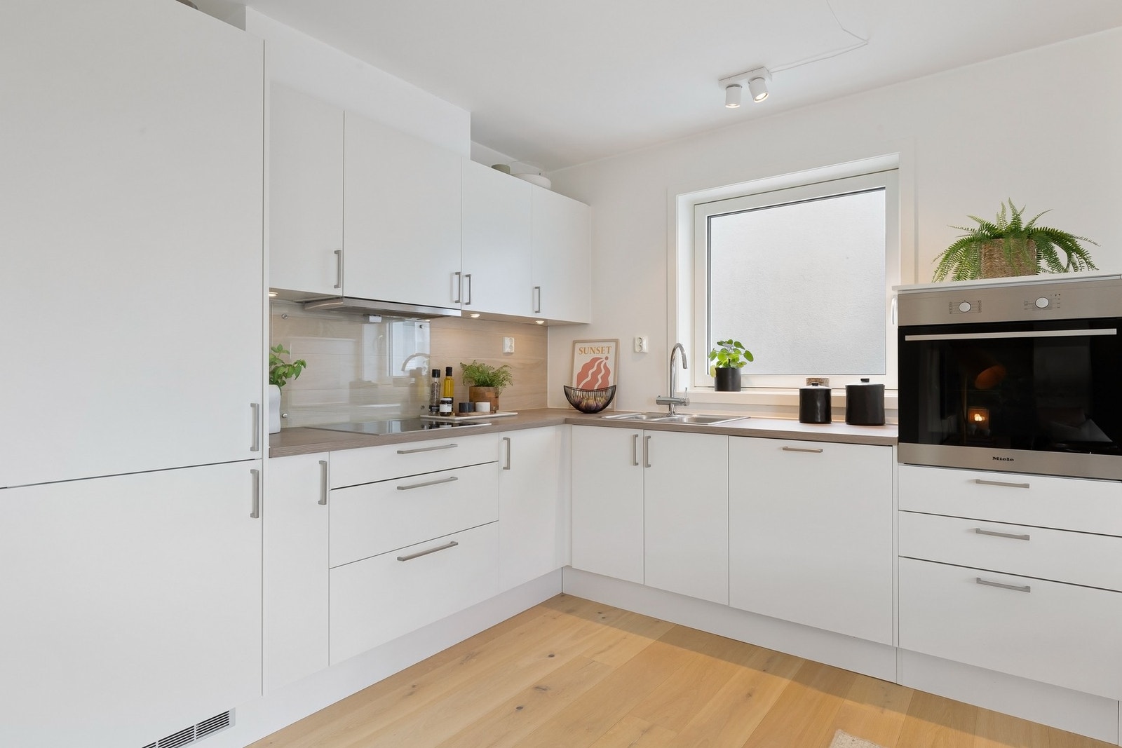 Kjøkkenet ligger åpent tilknyttet stuen og fremstår moderne og stilrent med hvite, glatte fronter og integrerte løsninger. Innredningen har gode arbeidsflater og praktisk oppbevaring i både over- og underskap. Galleribilde