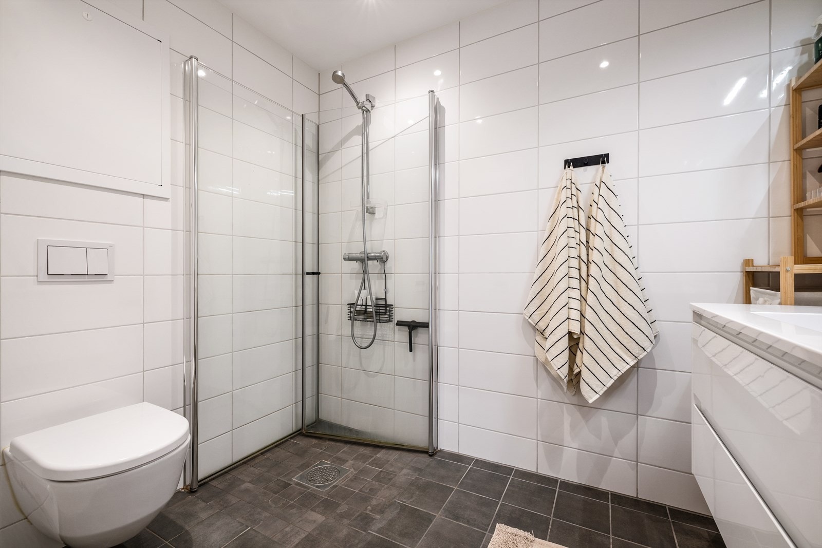 Helfliset bad med dusjhjørne, vegghengt toalett, servant med underskap og speil. Galleribilde