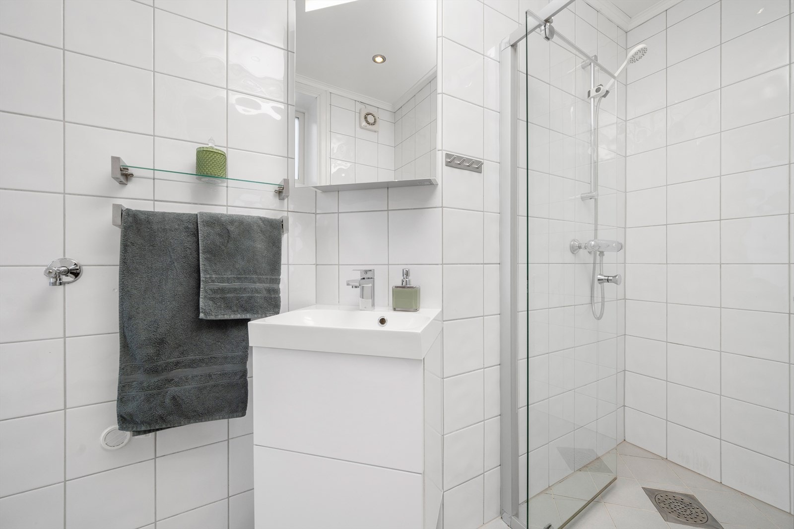 Badet er innredet med dusjvegger av glass og dusjgarnityr på vegg, toalett, innredning med servant, opplegg for vaskemaskin (Kran og avløp) Galleribilde