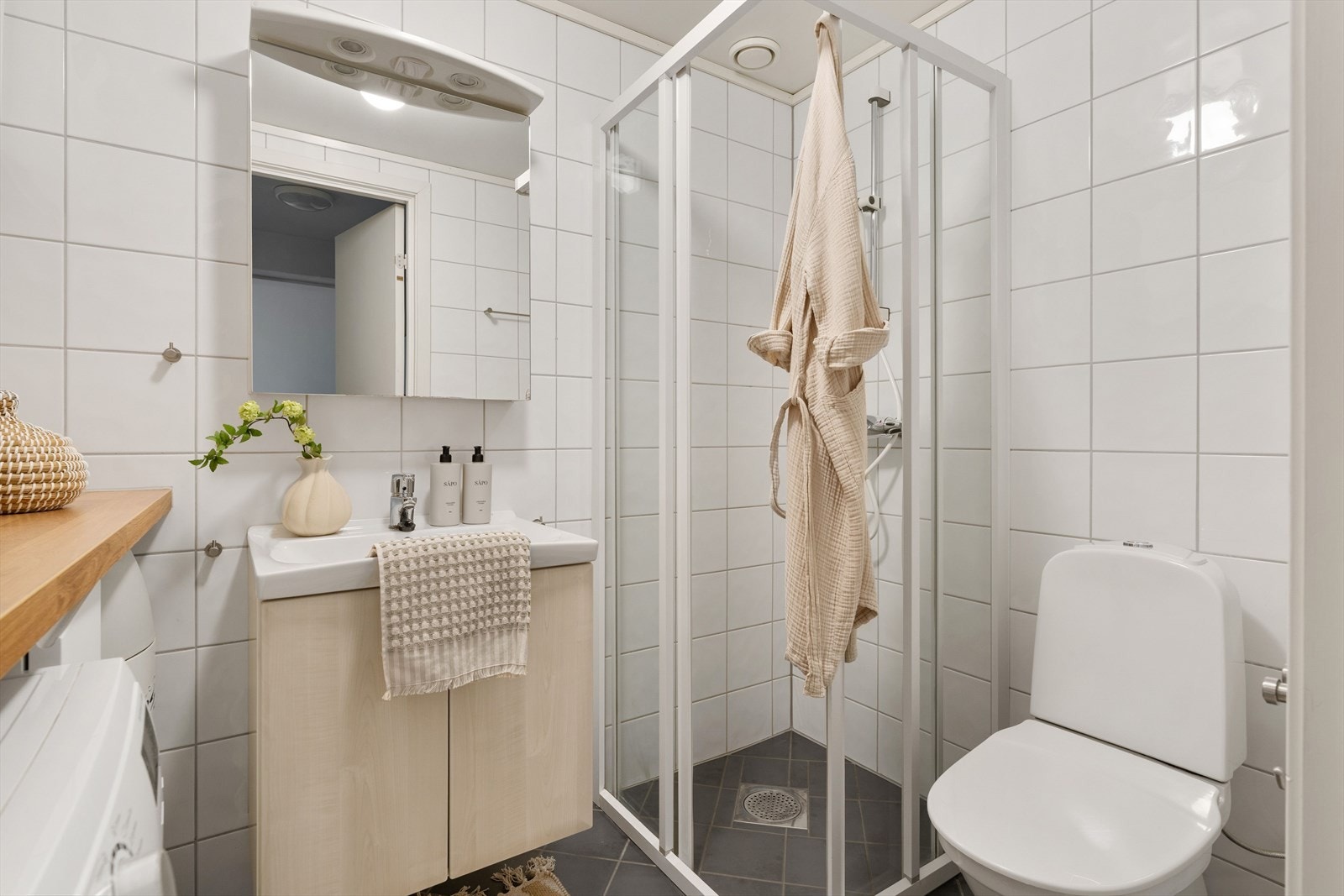 Badet er målt til 3,8 kvm og har flislagte vegger og gulv i et kontrastbasert fargevalg med hvite fliser på vegg og mørke fliser på gulv. Galleribilde