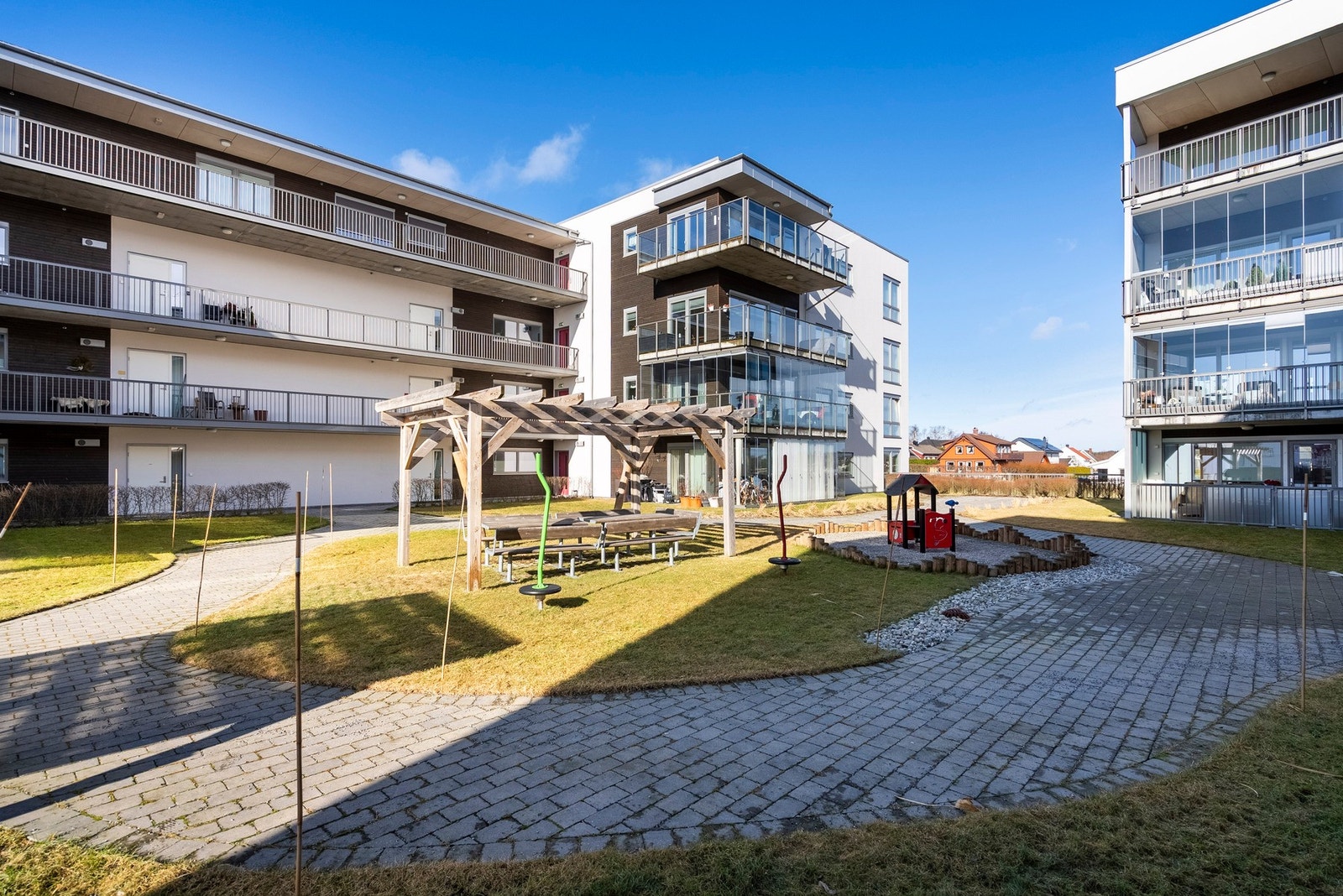 Fellesområdene ligger som et atrium mellom byggene og har et lite lekeområde for de minste og pergola for en hyggelig prat Galleribilde