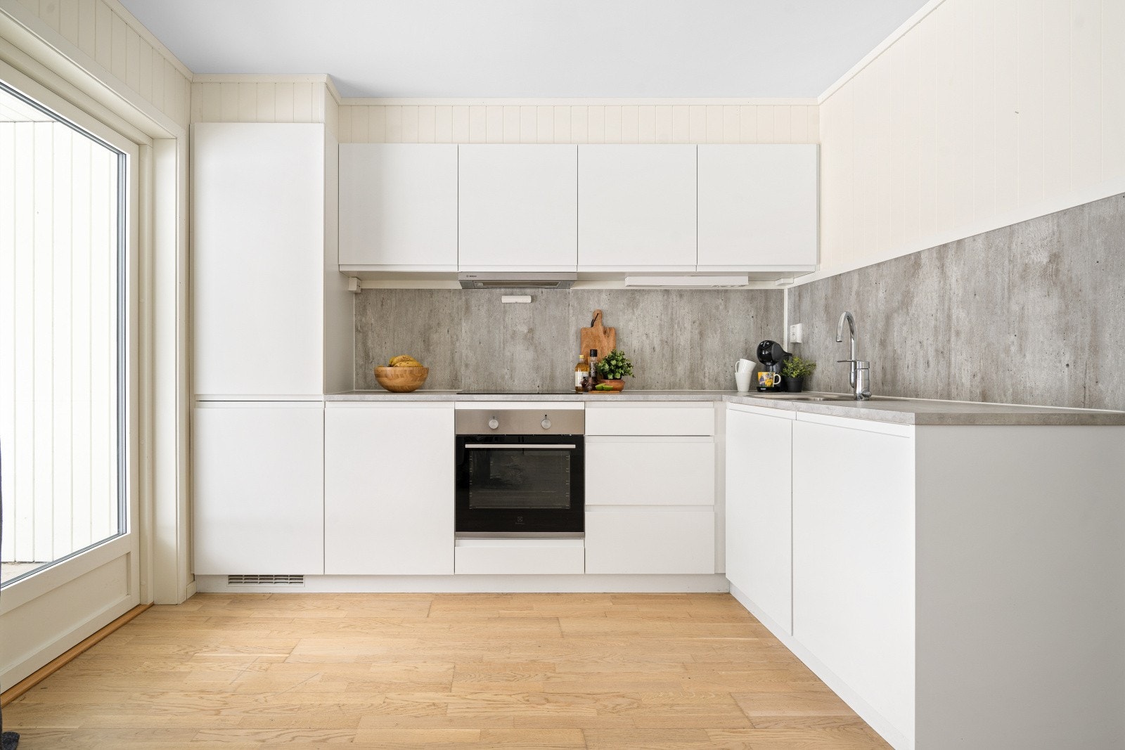 Lys kjøkkeninnredning med integrerte hvitevarer som koketopp, stekeovn, oppvaskmaskin og kombinert kjøl-/fryseskap. Galleribilde