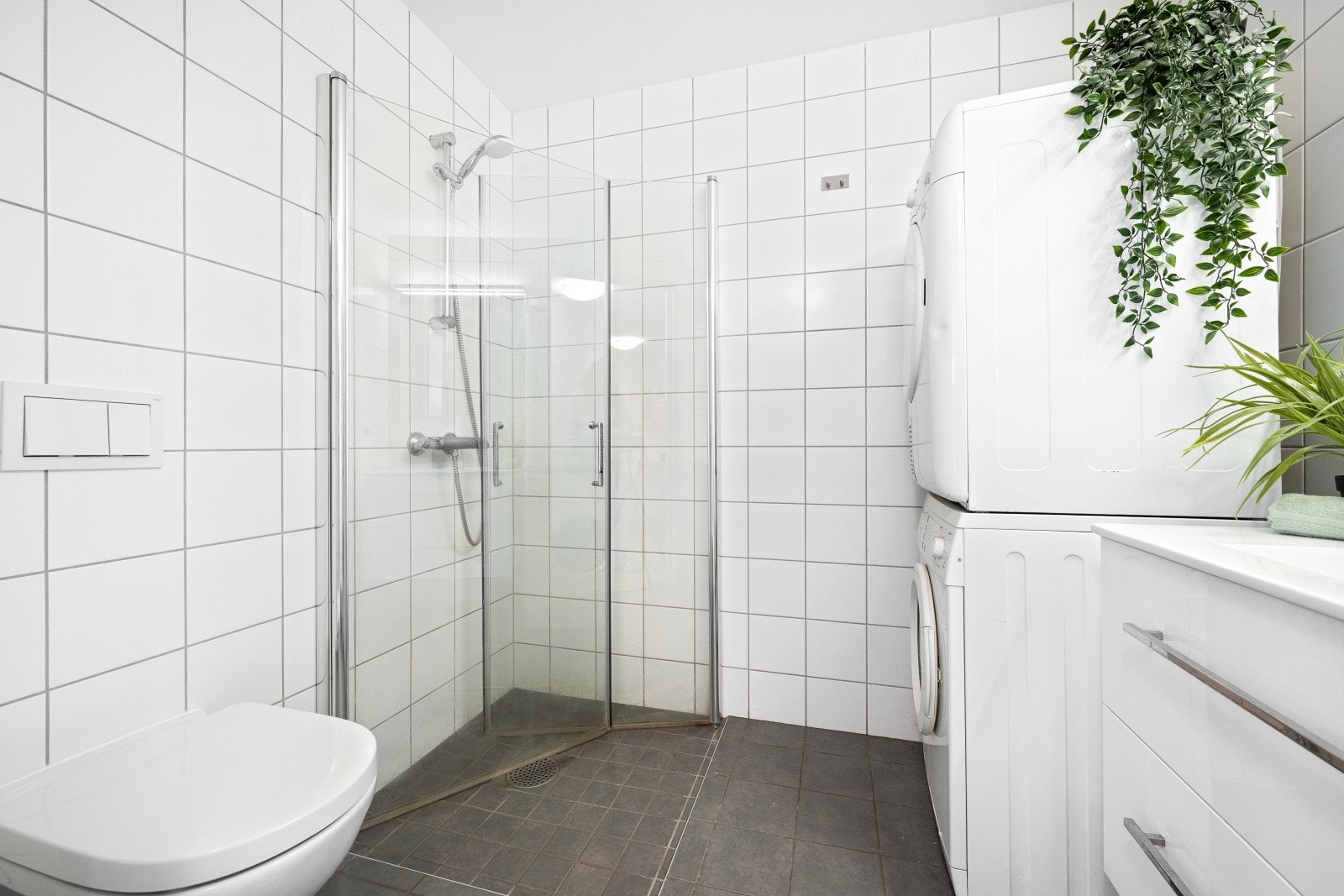 Baderommet har dusjhjørnet med glassdører, opplegg for vaskemaskin og vegghengt WC. Galleribilde