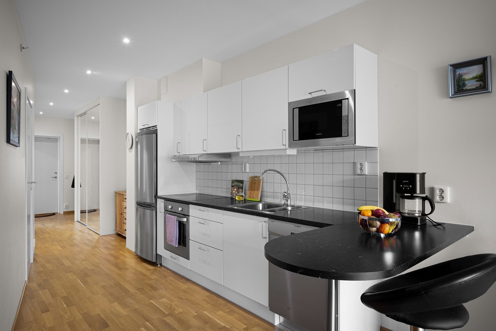 Pent kjøkken i hvit utførelse og med god skapplass, fliser over benken. Innebygd komfyr, platetopp og mikrobølgeovn. Oppvaskmaskin og kjøl-/fryseskap medfølger også.
Kjøkkenet har en kjekk barløsning. Galleribilde