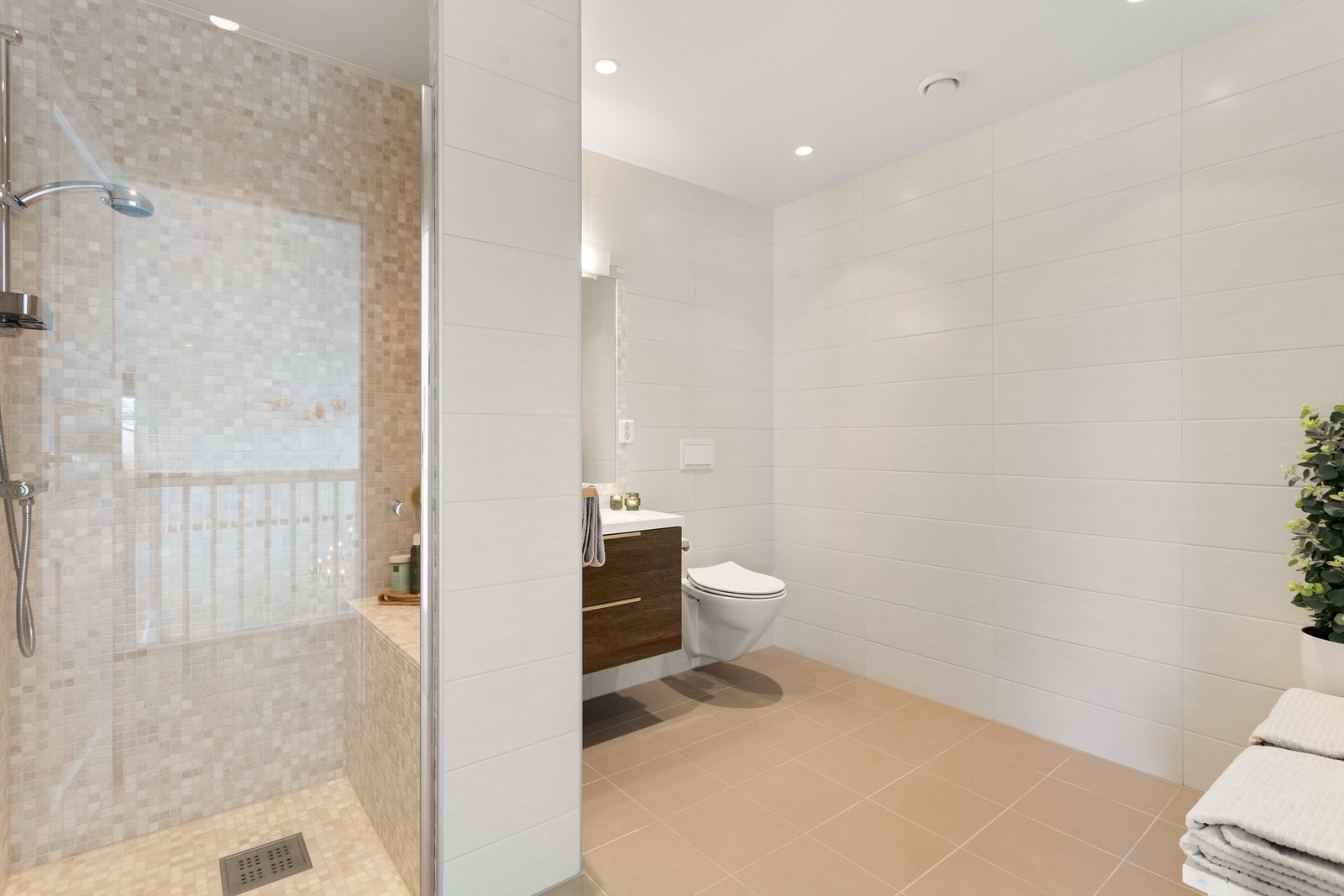 Badet har dusjnisje med dusjdør av glass og flislagt benk Galleribilde