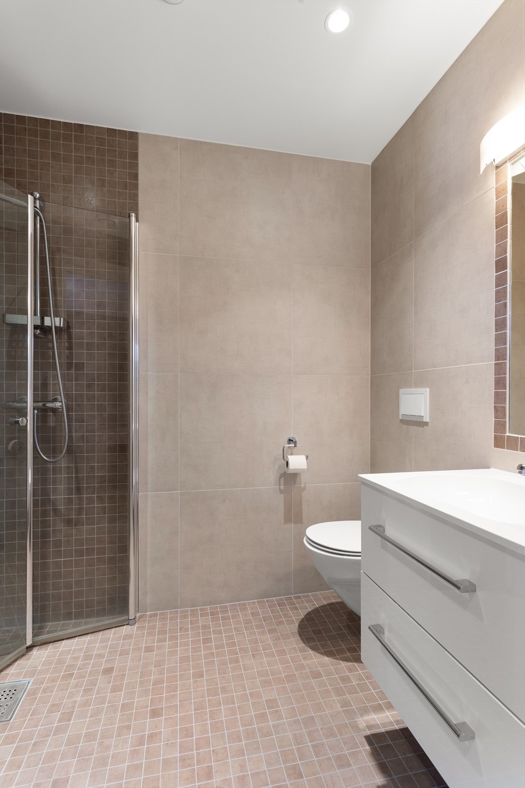 Pent flislagt bad med downlights i tak, gulvvarme og dusjhjørne som har foldedører av glass Galleribilde