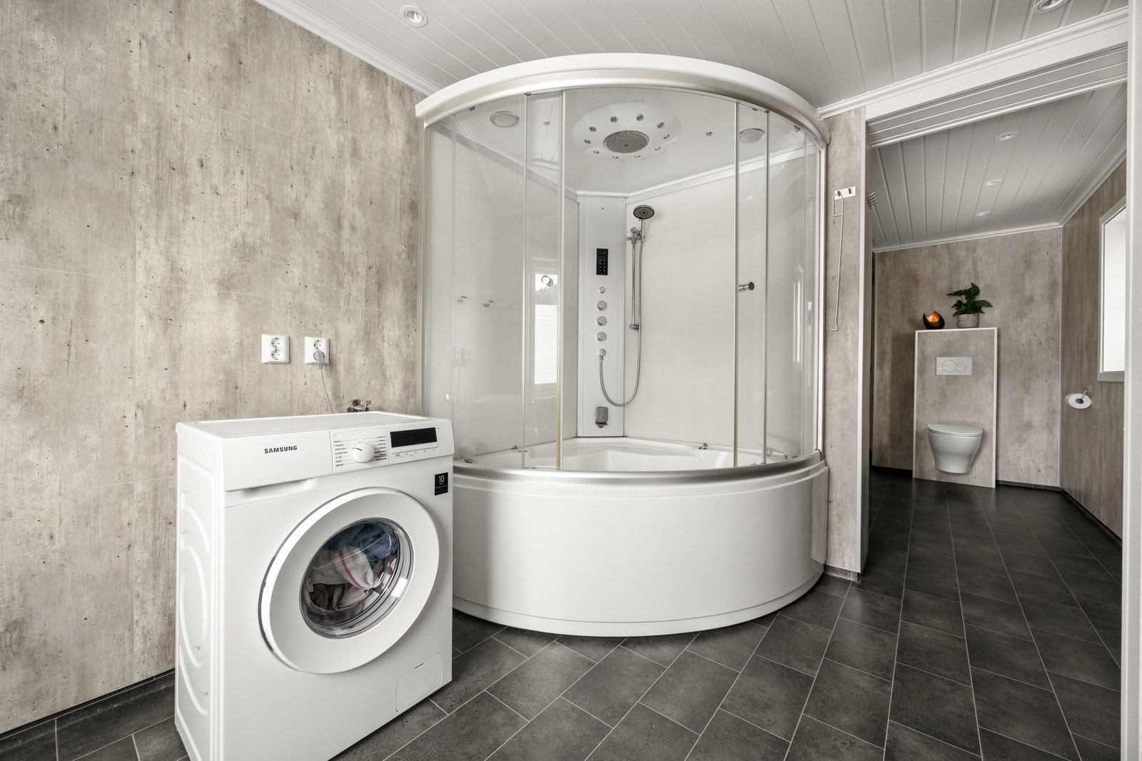 Badet er utstyrt med dusjkabinett, servantskap, veggmontert toalett og opplegg for vaskemaskin Galleribilde