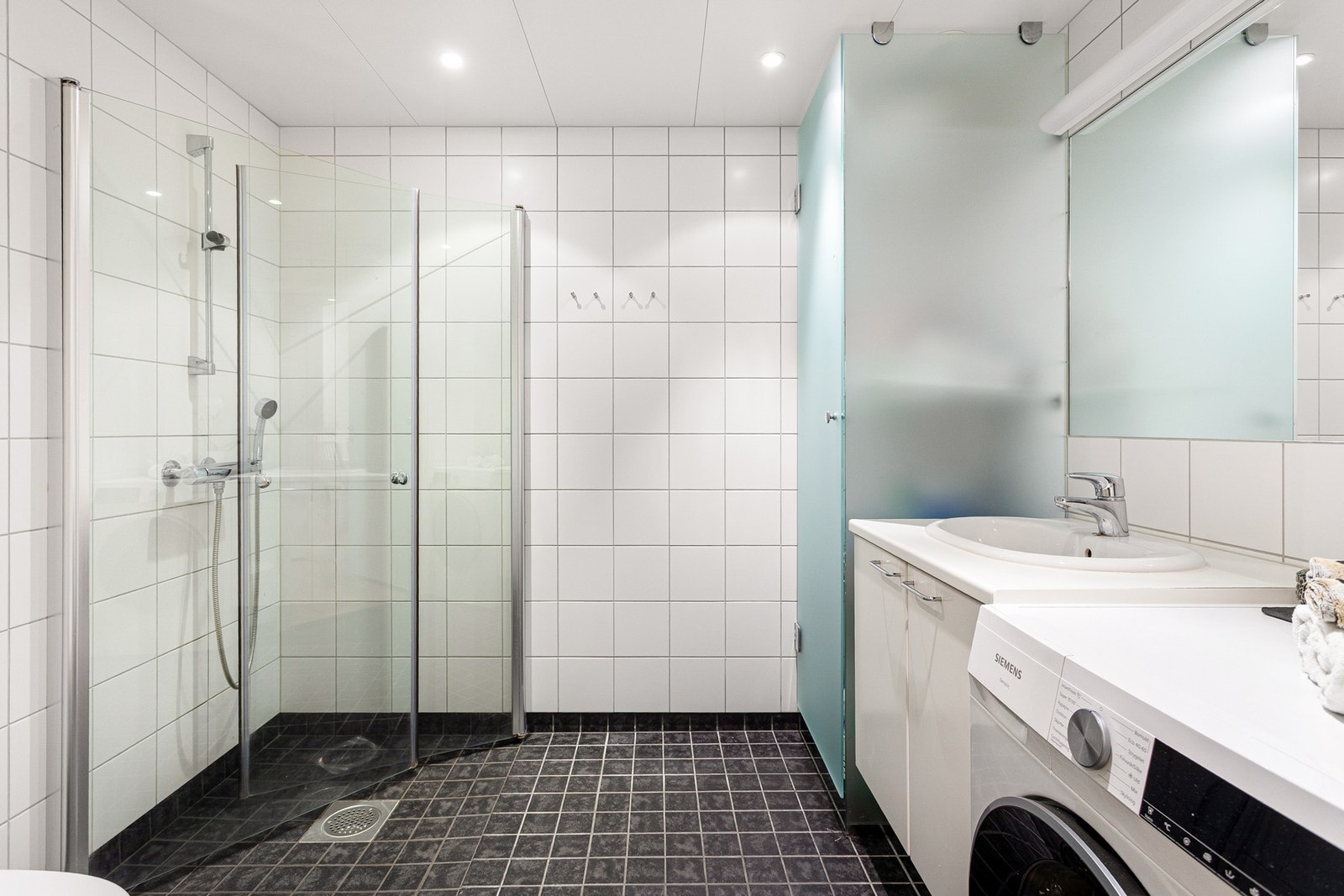 Pent flislagt baderom med varme i gulv og downlights i himling. Dusjhjørne med innfellbare glassdører frigjør plass på gulvet. Galleribilde