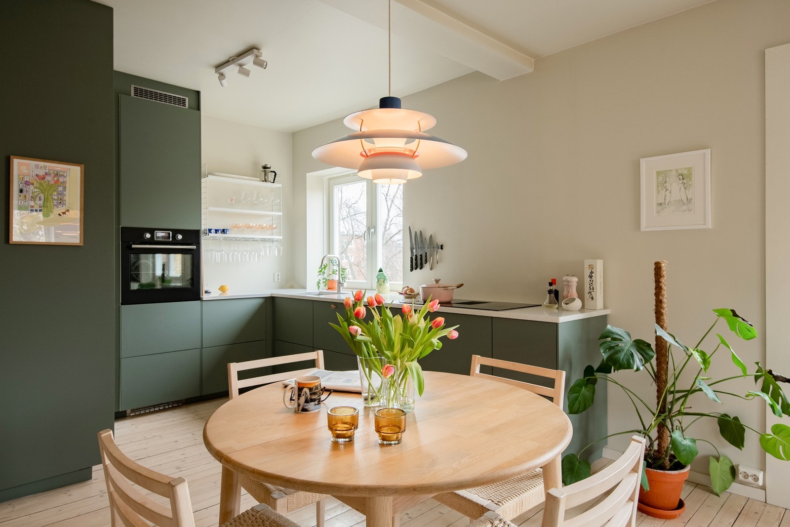 Kjøkkenet har moderne, slette fronter i en dempet grønnfarge, kombinert med lyse benkeplater som gir et elegant uttrykk. Galleribilde