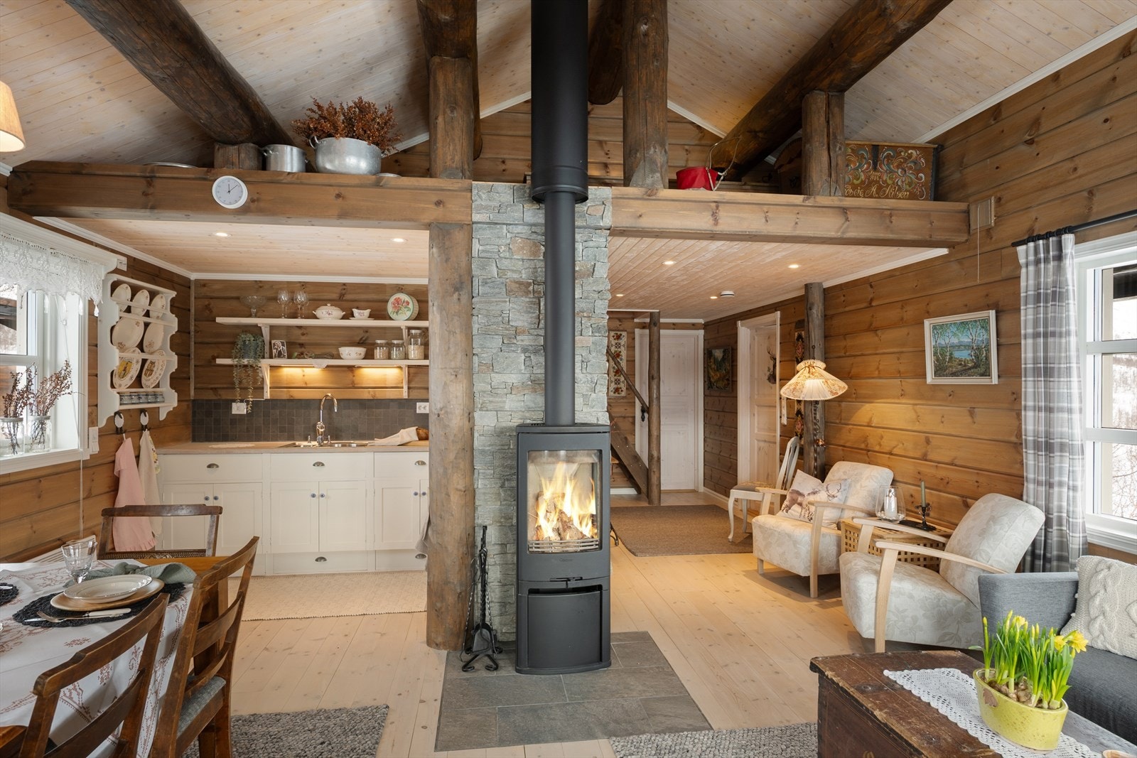 Den åpne stue- og kjøkkenløsningen er hyttas sosiale samlingspunkt, med en sentralt plassert peisovn. Galleribilde