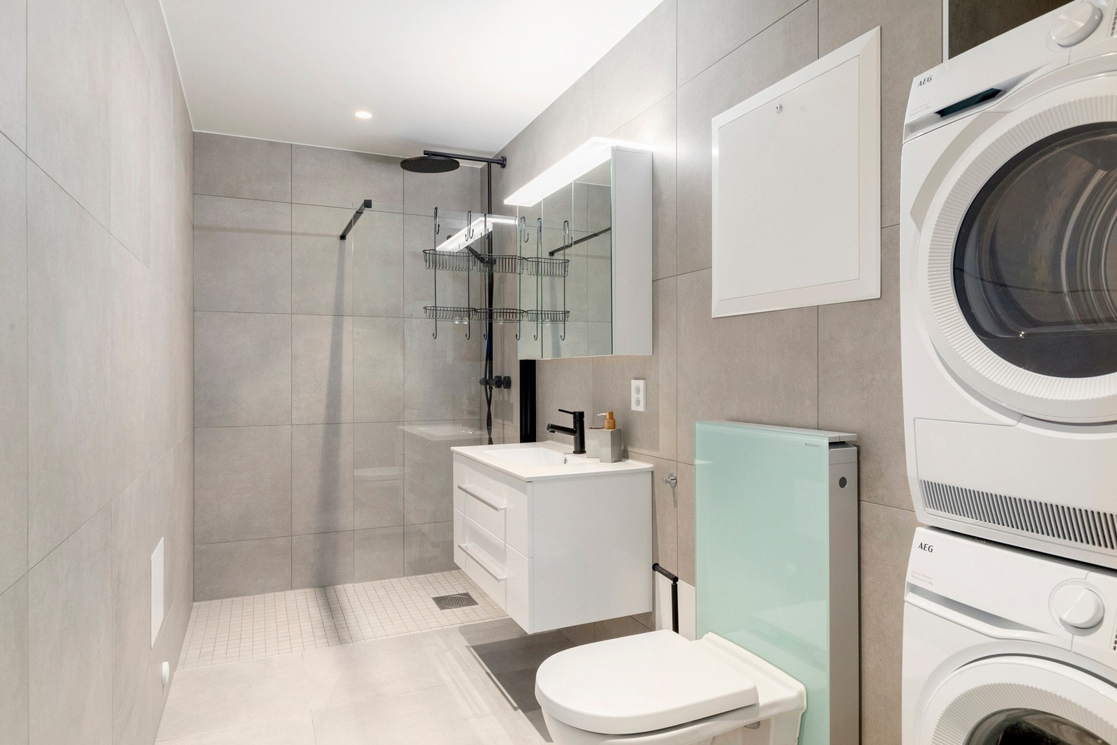 Delikat flislagt bad med stor dusjsone med regnfallsdusj og baderomsinnredning med porselensvask. Galleribilde