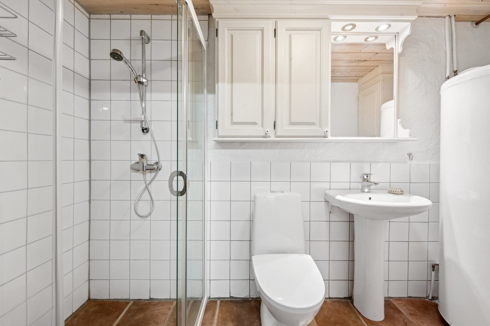 Badet i hyttas underetasje er praktisk og funksjonelt. Her finner du en baderomsinnredning med en stående servant, toalett og dusj med glassdører. Galleribilde