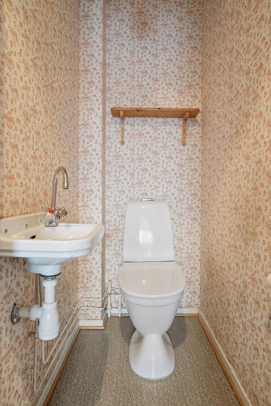 Separat wc-rom med gulvstående toalett og enkel servant på vegg. Galleribilde