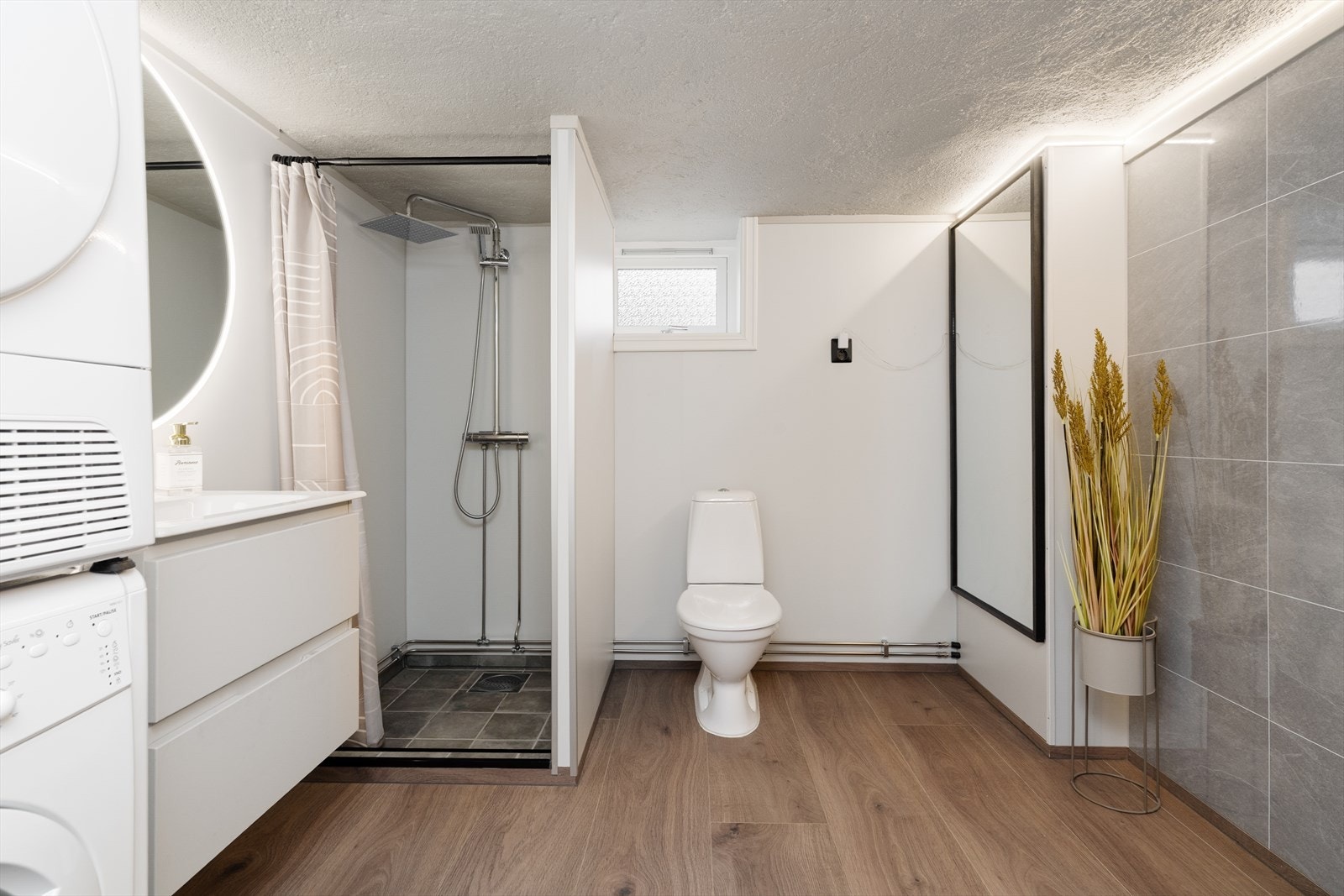 Kombinert bad- og vaskerom i kjeller, pent pusset opp som egeninnsats av selger i 2025. Badet har toalett, dusjnisje med forheng og opplegg for vaskemaskin. Galleribilde