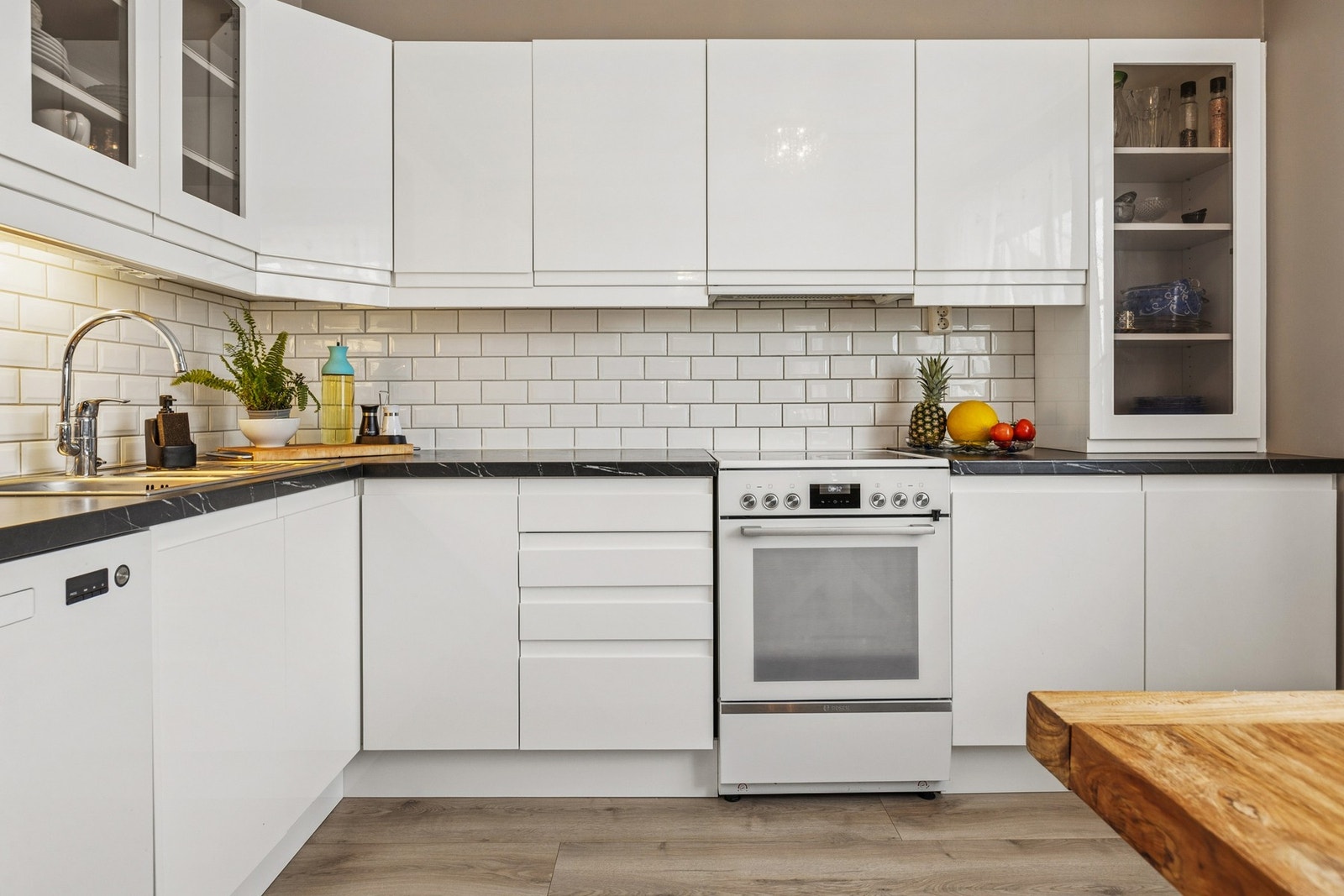 Kjøkkeninnredning med hvite høyglans fronter og laminert benkeplate. Fliser på vegg mellom kjøkkenbenk og overskap. Benkeskapsbelysning og stikkontakter under overskap. Nedfelt oppvaskkum av rustfritt stål med ett-greps armatur. Komfyr med keramisk platet Galleribilde