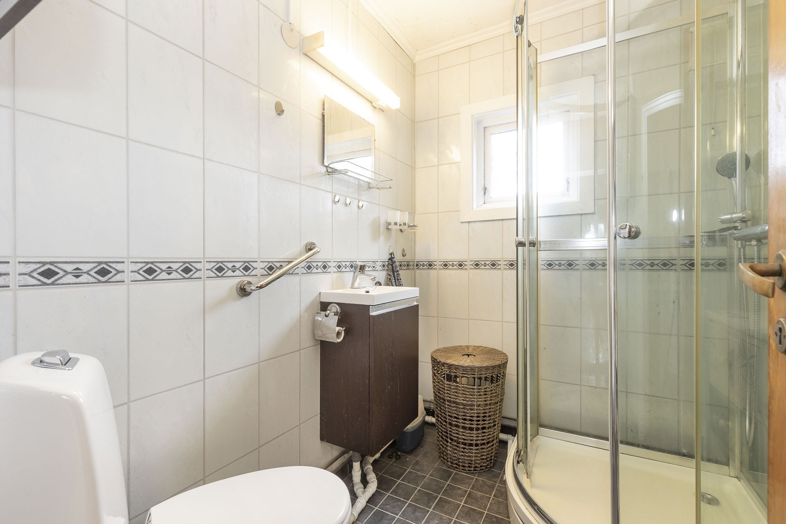 Flislagt bad med dusjkabinett toalett og liten innredning med servant. Galleribilde