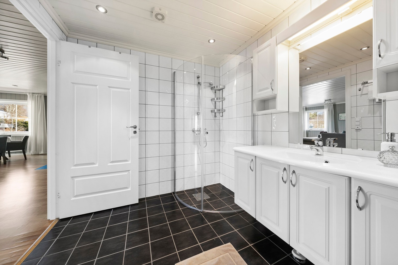 Romslig og praktisk flislagt bad med lyse fliser på veggene, mørkt gulv og god plass til oppbevaring. Galleribilde