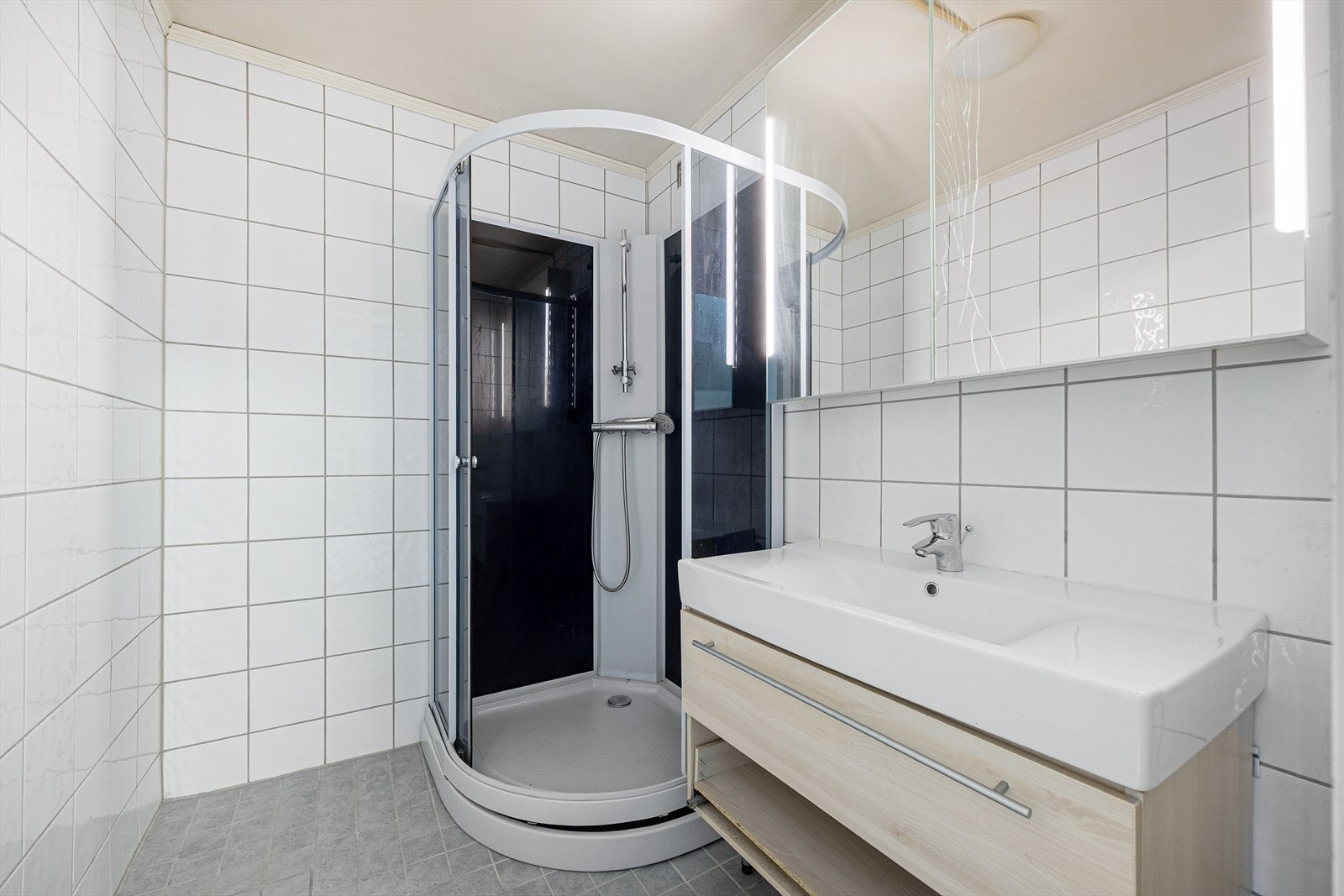 Leilighetens bad ligger i 2. etasje, med flis på vegger og gulv. Badet har innredning med nedfelt servant, speilskap og dusjkabinett.
Innredninger fremstår med noe skader. Galleribilde