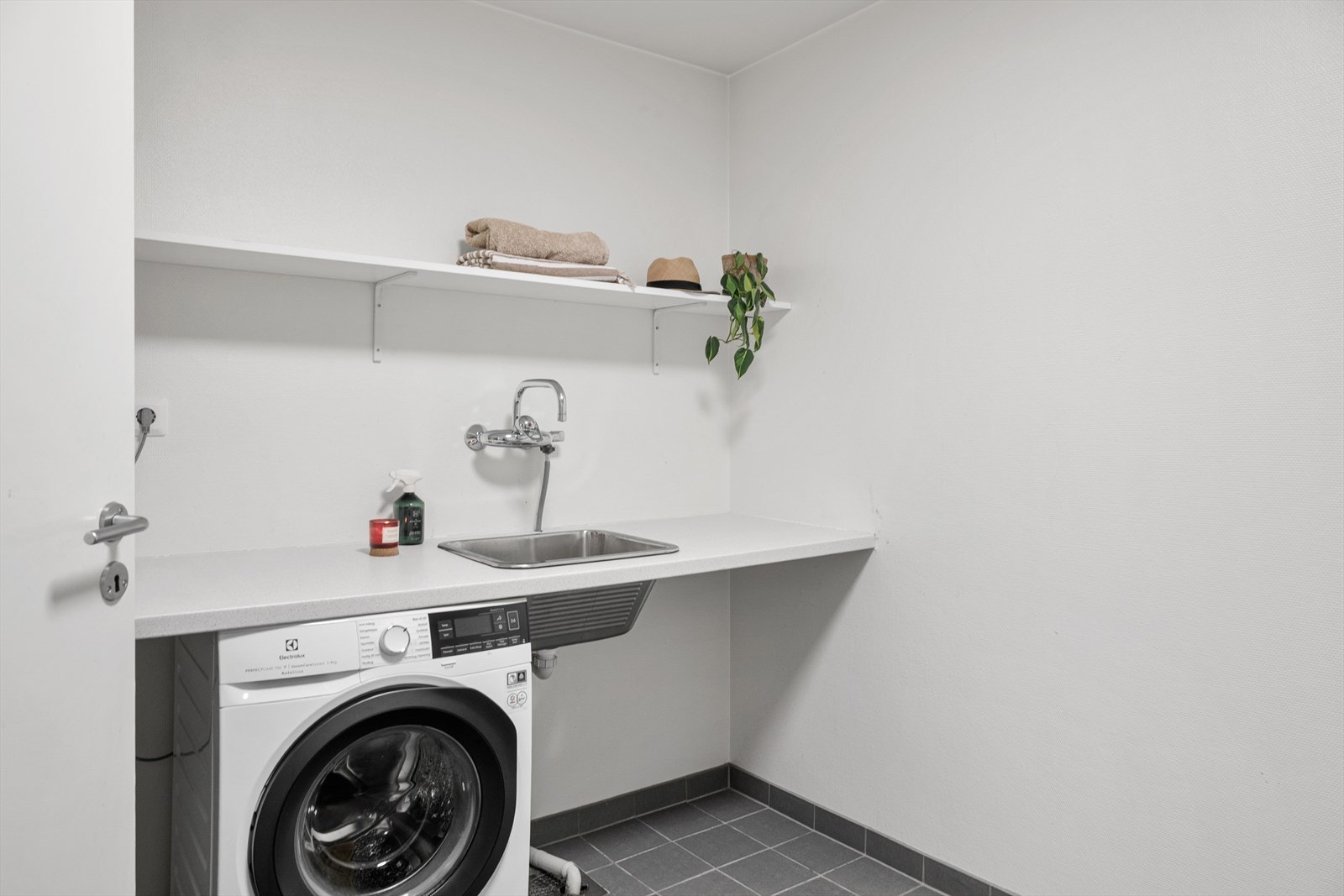 Rommet har fliser på gulvet, vegghengt toalett og åpen dusjløsning. Det er også opplegg for vaskemaskin samt god benkeplass som egner seg godt til å brette klær. Galleribilde