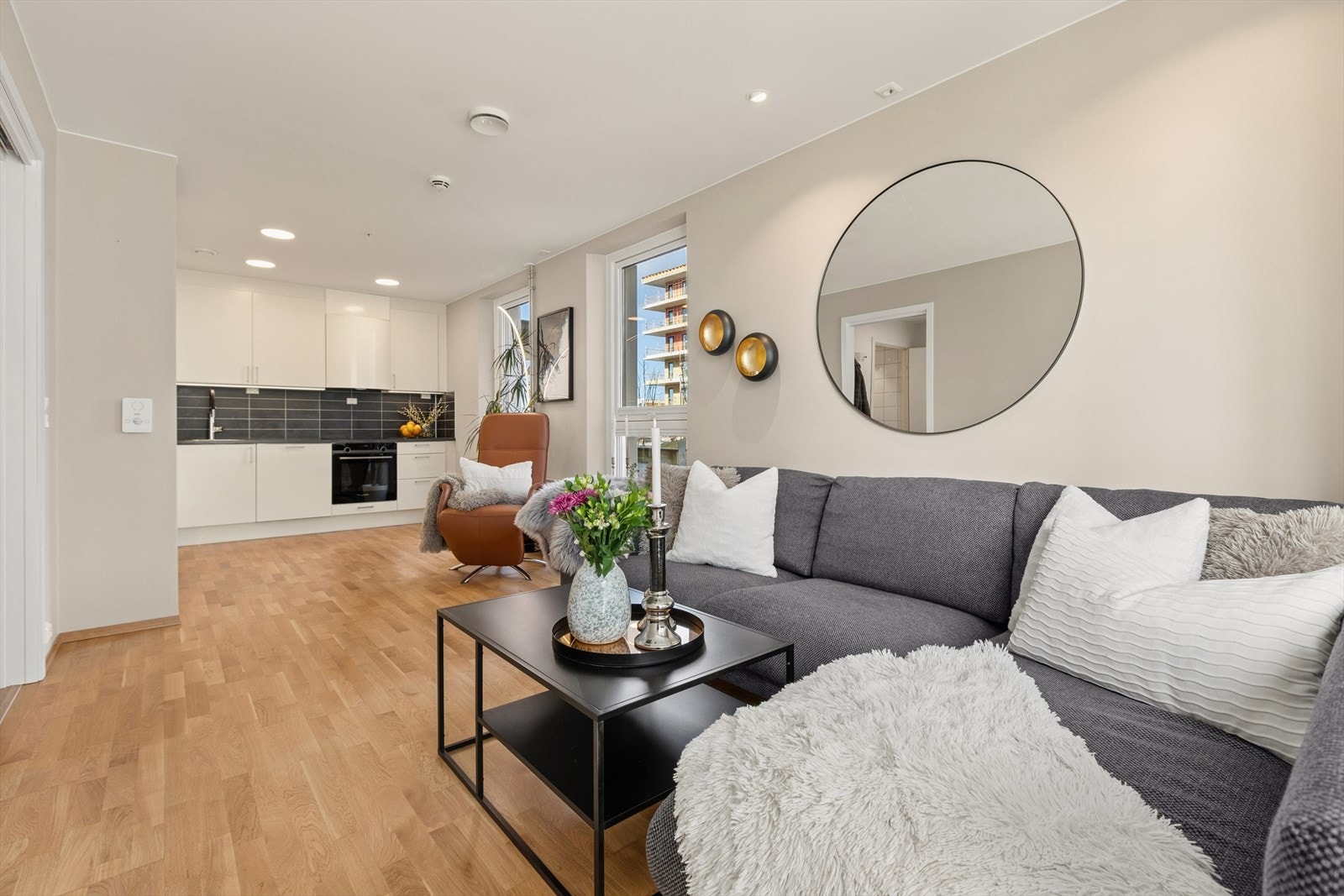 Leilighetens sosiale sone med stue og kjøkken ligger i åpen løsning. Et lyst og innbydende rom med store vindusflater og lysmalte veggflater med listefrie overganger mellom vegger og tak, samt rundt vinduer. Galleribilde