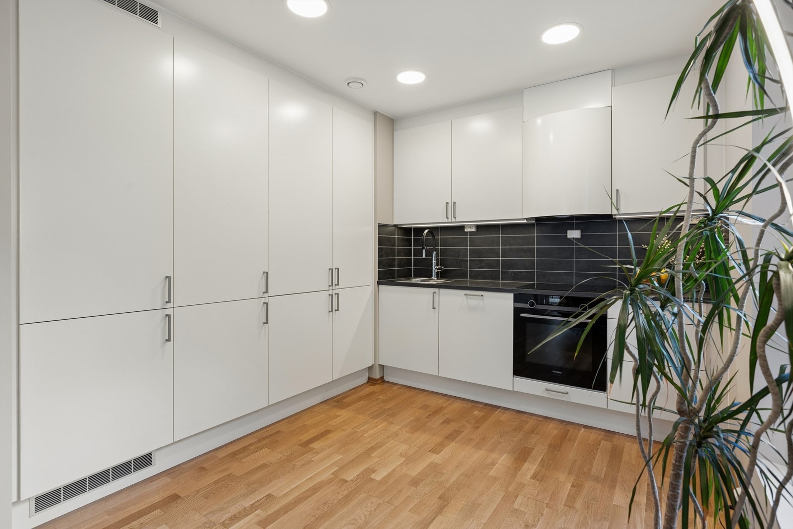 Kjøkkenet er stilrent innredet med hvite, slette fronter og grå benkeplate i laminat. Et godt utnyttet kjøkken hvor man har rikelig med lagringsplass i skap. Galleribilde