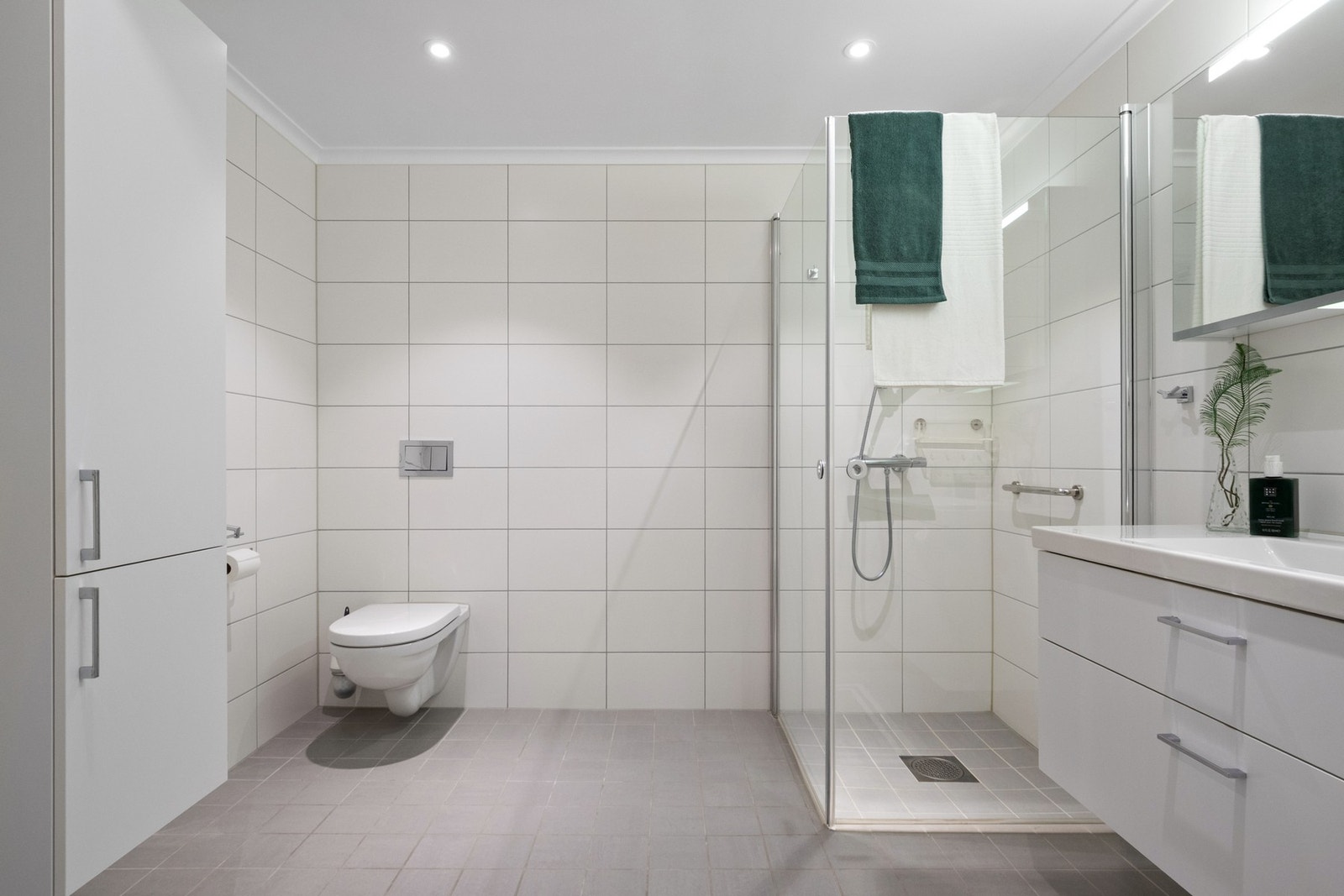 Badet er flislagt med gulvvarme og fremstår funksjonelt med dusjløsning og moderne innredning. Det er opplegg for vaskemaskin og vegghengt toalett som gir et ryddig uttrykk. Galleribilde
